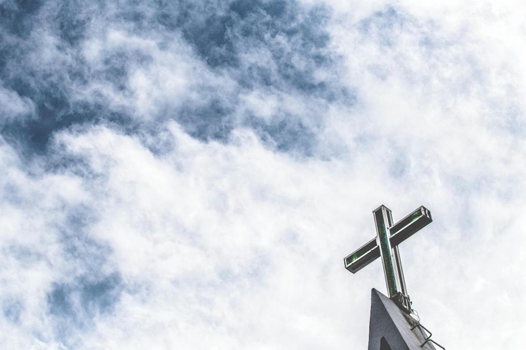 A vibrant cross atop a church steeple with a backdrop of a cloudy sky.